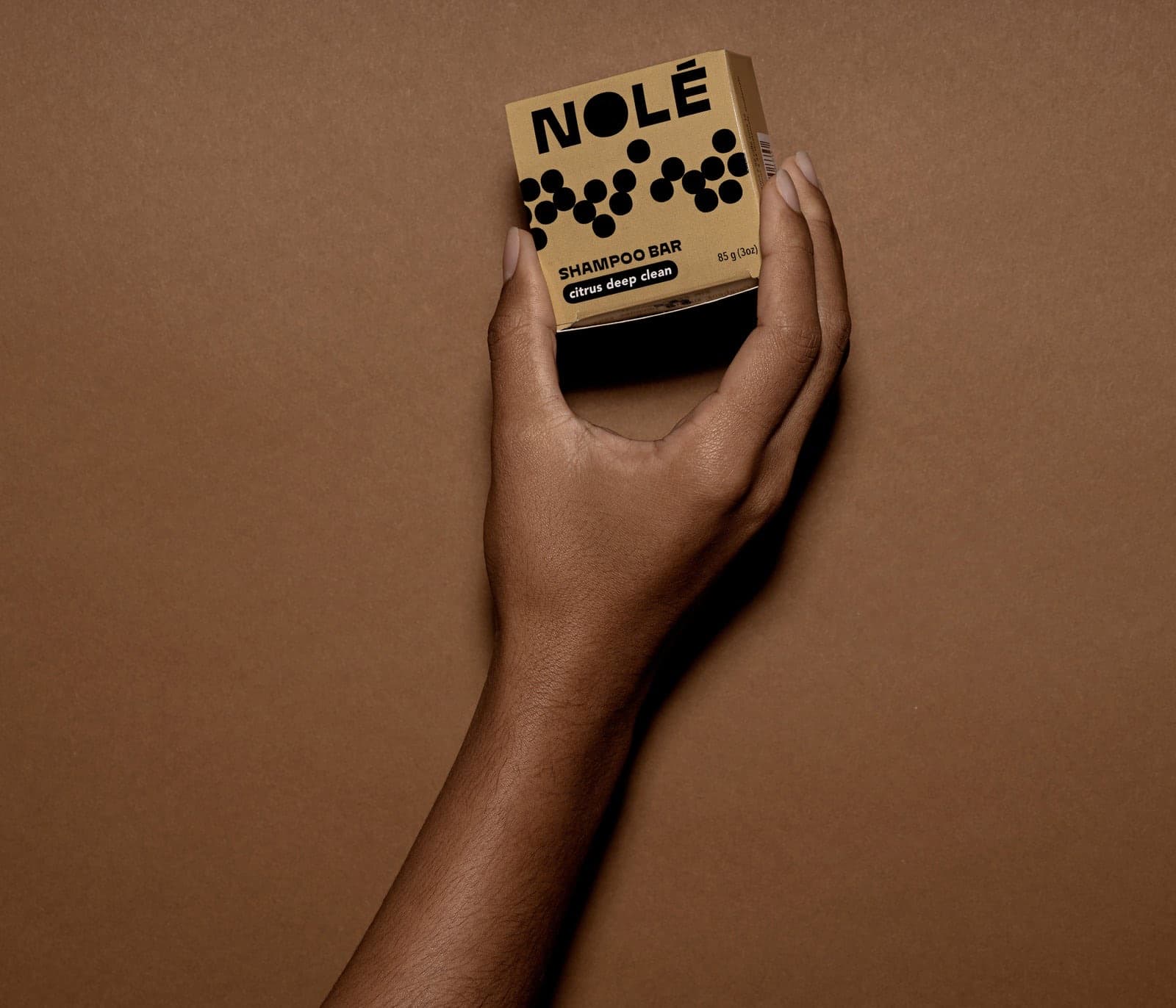 A hand holding a NOLÉ shampoo bar box